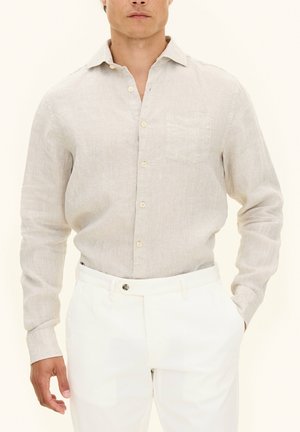 Ljus beige långärmad skjorta i texturerad tyg, med knäppning fram och bröstficka, kombinerad med vita byxor.
