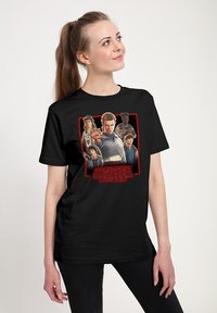 Zwart katoenen T-shirt met een kleurrijke "Stranger Things"-afbeelding met personages, gedetailleerde gezichtsuitdrukkingen en een gedurfde rode rand.