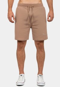 Pantaloni corti beige da uomo realizzati in tessuto testurizzato, con una cintura elastica con coulisse e tasche laterali, arricchiti da un logo.