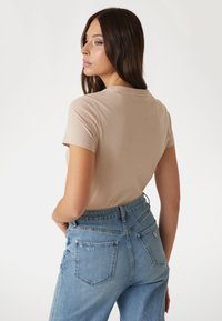 Camiseta ajustada beige de manga corta, combinada con jeans de mezclilla azul de cintura alta que presentan un parche con logo y bolsillos traseros.