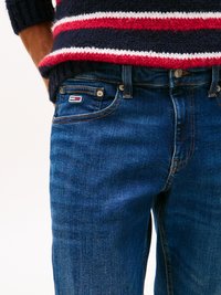 Sötétkék farmernadrág finom kopással, standard övhurkokkal és kis logóval a frontzsebben. Csíkos kötött pulóverrel párosítva.