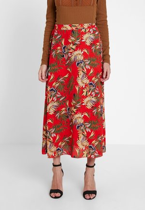 Red midi skirt with tropical floral print worn with brown long-sleeve top and black ankle-strap heels on white background.