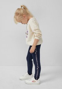 Crème sweatshirt met bloemenontwerp, marineblauwe legging met bedrukte tekst en witte sneakers. De tekst luidt: "je bent geweldig." Casual outfit.