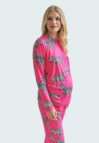 Růžový top s dlouhými rukávy a odpovídajícími kalhotami, které mají černobílé pruhy jako zebra. Hladká textura, volný střih a pohodlný design.