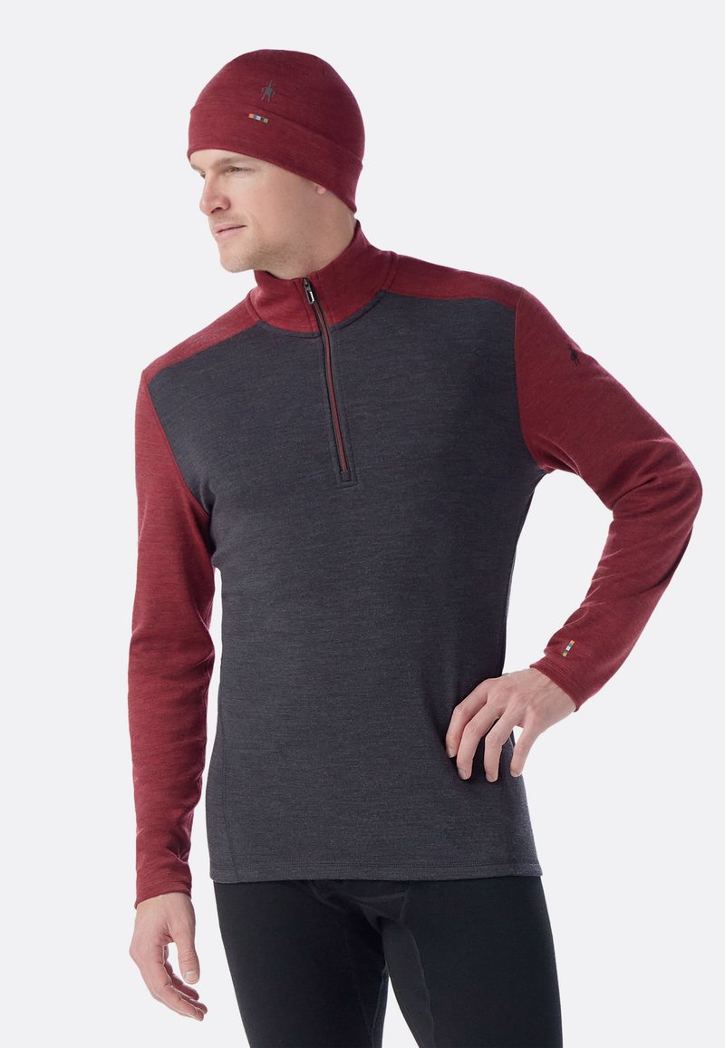 Donkere grijze longsleeve pullover met rode raglanmouwen, voorzien van een ritssluiting bij de kraag en logo-accenten op de borst en mouw.