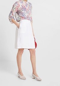 Leichte, mehrfarbige Tierdruckbluse mit langen Ärmeln; weißer Leinen A-Linien-Rock mit Taschen; weiße perforierte Pumps; rote Handtasche.