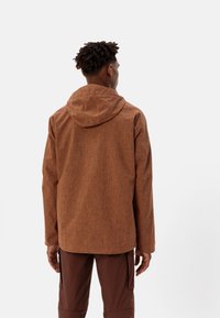 Giacca con cappuccio marrone, texturizzata, dal taglio rilassato e con spacco posteriore, abbinata a pantaloni marroni coordinati.