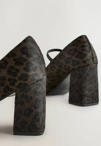 Paire de chaussures à talons hauts imprimé léopard marron avec talons larges et une bride sur le dessus, présentées sur fond blanc.