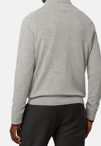 Maglione grigio a maglia con colletto alto, polsini e orlo a coste. Tessuto morbido con una vestibilità comoda, indossato con pantaloni grigio scuro.
