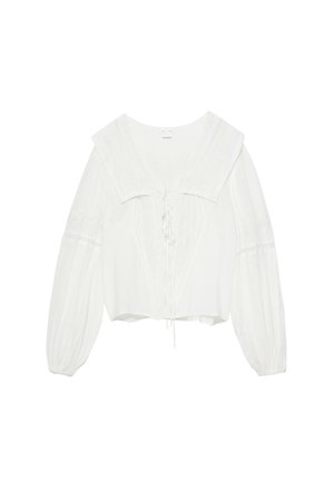 Blouse blanche à manches longues avec large col, détails en dentelle, poignets froncés et fermeture à nouer devant, présentée sur un fond uni.