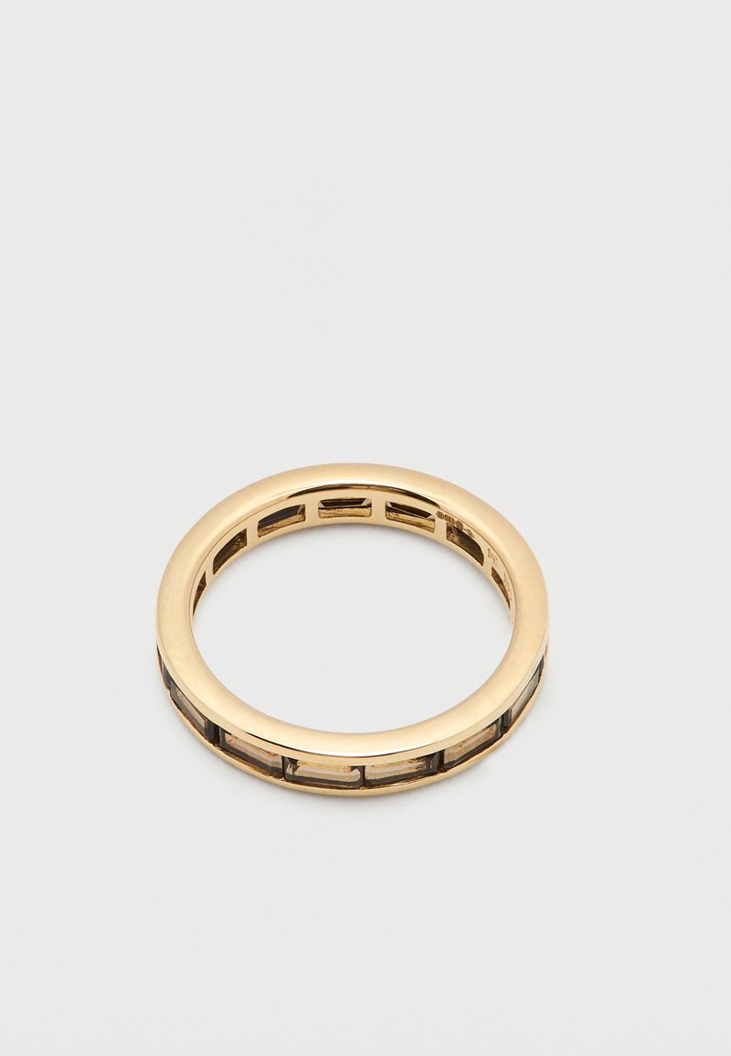 Arany gyűrű sima külsővel és kivágott geometriai mintákkal a szíjon, váltakozó tömör és áttetsző részekkel.