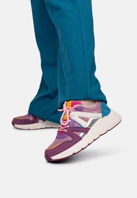 Multicolored sneaker featuring mesh and suede materials, purple and pink hues, and a reflective silver accent. Laces are light pink.
