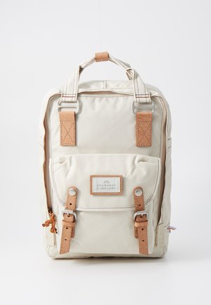 Beige szövet hátizsák barna bőr részletekkel, felső fogantyúkkal, egy elülső zsebbel és ezüst színű fém kiegészítőkkel. Jellegzetes a minimalista dizájnja miatt.