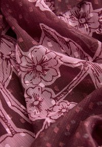 Palaidi audinys su bordo fono, turintis didelius rožinius gėlių raštus ir lengvą tekstūrą, kuri sukuria subtilų blizgesį ir sluoksniuotą išvaizdą.