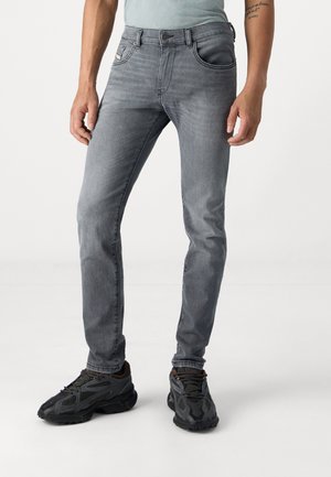Slim-fit gray denim jeans with a smooth texture, featuring five pockets and a subtle logo on the front. Paired with dark athletic shoes.