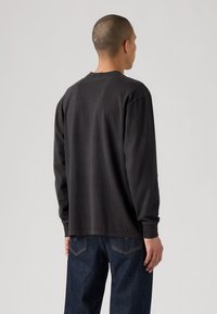 Schwarzes Baumwoll-T-Shirt mit langen Ärmeln, rundem Halsausschnitt, lässiger Passform und schlichter Textur. Kombiniert mit dunkelblauen Jeans.