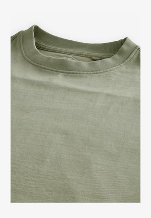 Világos olíva zöld póló, puha pamutból készült. Klasszikus kerek nyakkivágással és sima, kissé texturált anyaggal rendelkezik.