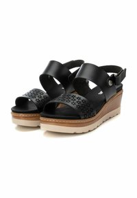 Sandalias de cuña de cuero negro con diseño perforado en la correa, correa ajustable en el tobillo y suela de plataforma beige.
