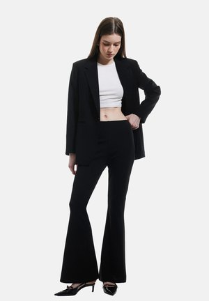 Svart skräddarsydd blazer över en vit croptop, matchad med svarta utsvängda byxor och svarta högklackade skor. Slät tyg, strukturerad passform, minimalistisk stil.