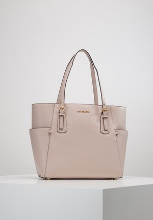 Sac cabas en cuir beige Michael Kors avec doubles anses d'épaule, ferrures dorées et poches latérales, présenté sur un piédestal blanc.
