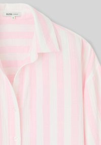 Chemise oversize légère à rayures alternées rose et blanche. Dotée d'un col et d'une fermeture à boutons sur le devant.