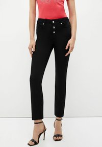 Jeans ajustados negros con cinco botones en la cintura, bolsillos frontales y un diseño de pierna recta. Combinados con sandalias de tacón alto negras con tiras.