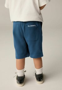 Plave pamučne kratke hlače s stražnjim džepom s 'ALLSAINTS' logotipom. Uparene s crnim tenisicama i bijelim čarapama do gležnja. Jednostavan dizajn, ležeran kroj.