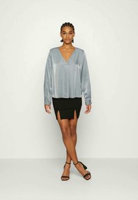 Blusa de cetim cinza claro com mangas longas e decote V, combinada com uma saia mini preta com fendas frontais e saltos pretos com tiras.