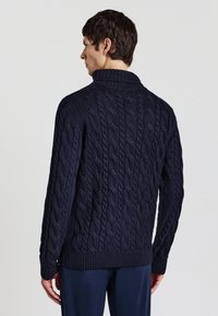 Maglione navy a trecce con colletto alto e orlo a coste. Motivo testurizzato su tutta la superficie. Modello mostrato di spalle.