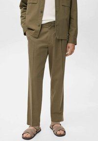 Pantalones verde oliva de corte relajado con una textura suave. Cuentan con bolsillos laterales y cierre de botón. Se combinan con sandalias marrones.