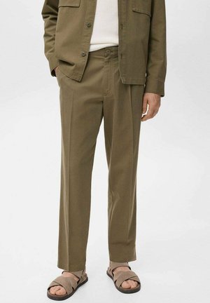 Olive green trousers in a relaxed fit with a smooth texture. Features side pockets and a button closure. Paired with brown sandals.