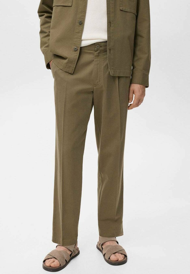 Pantalones verde oliva de corte relajado con una textura suave. Cuentan con bolsillos laterales y cierre de botón. Se combinan con sandalias marrones.
