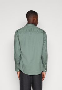 Chemise verte à manches longues en tissu lisse, avec un col, des poignets boutonnés et un ourlet arrondi, vue de l'arrière.