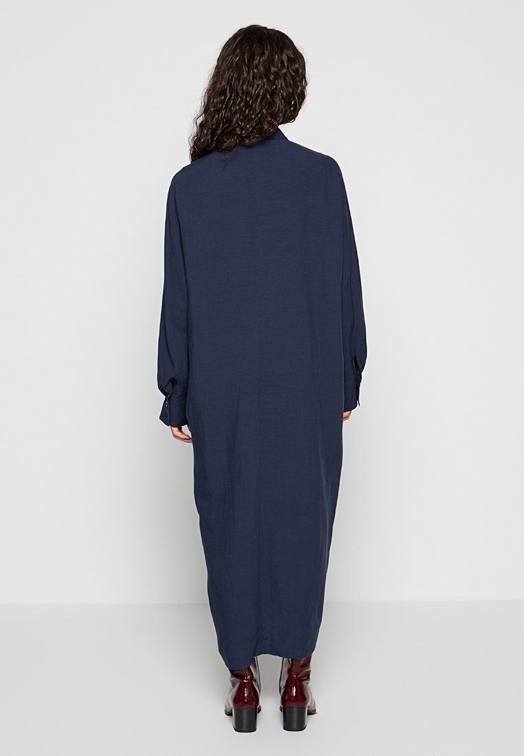 Abito blu navy a maniche lunghe con una vestibilità ampia, dotato di polsini con bottoni, una scollatura alta e una silhouette dritta, abbinato a stivaletti con tacco.