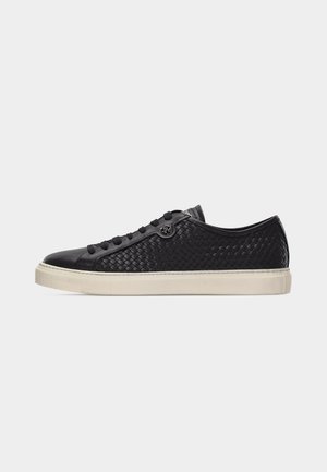 Low-top black woven leather sneaker with black laces and white rubber sole, shown in right side profile on light gray background.