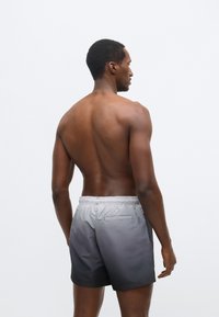 Αντρικό μαγιό σορτς με διαβαθμισμένο σχέδιο, που μεταβαίνει από ανοιχτό γκρι σε σκούρο γκρι, κατασκευασμένο από απαλό, ελαφρύ ύφασμα με ελαστική μέση.