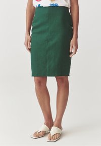 Gonna a matita verde in lino con design aderente, lunghezza al ginocchio e texture liscia. Abbinata a sandali slip-on di colore avorio.