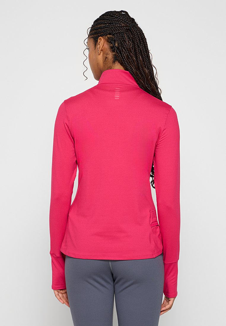Camiseta deportiva de manga larga en un vibrante color rosa, con un alto cuello, un diseño ajustado y agujeros para los pulgares. Textura suave con detalles de hardware mínimos.
