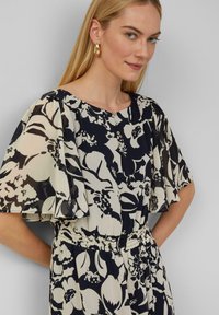 Blumengemustertes Kleid in Marineblau und Creme, mit kurzen Glockenärmeln, einem runden Ausschnitt und einem elastischen Bund für besseres Tragen.