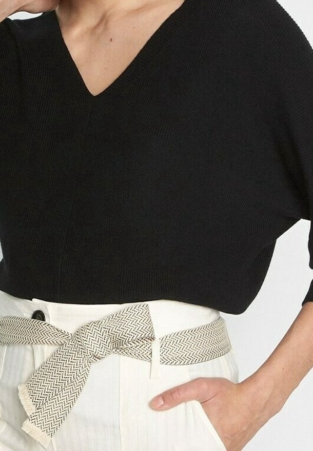 Czarna dzianinowa bluzka z dekoltem w serek i luźnym krojem, noszona z jasnymi, wysokimi spodniami z paskiem w wzór rybiej ości.