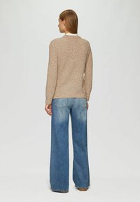 Beige Strickpullover mit langen Ärmeln, Rundhalsausschnitt und strukturiertem Finish, kombiniert mit hellblauen weiten Jeans.