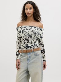 Top off-the-shoulder in tessuto leggero con macchie nere e marroni, abbinato a jeans di denim chiari a vita alta e una cintura marrone.