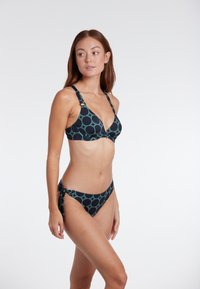 Bikiny set s trojuholníkovým vrchom a nízkym spodkom v námorníckej modrej farbe so zaoblenými tyrkysovými vzormi; obsahuje nastaviteľné ramienka a detail na viazanie na boku.