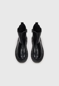 Zwarte leren enkelschoenen met een ronde neus, elastische zijkanten en een textuur van rubberen zool, met een gestikt accent langs de zool.