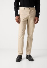 Beige cotton trousers with a straight cut, featuring front pockets and a button closure. Paired with black shoes.