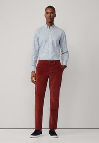 Camisa a rayas azul y blanca con cuello tipo button-down, combinada con pantalones de pana color óxido y zapatillas negras. Diseño sencillo, textura suave.