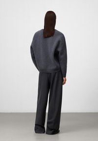 Grijze wollen trui met een ontspannen pasvorm, ribbelboord en verlaagde schouders, gecombineerd met een wijde, donkergekleurde broek. Soepele textuur, minimalistisch ontwerp.