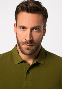 Polo de color verde oliva con cuello, presenta una tapeta de tres botones y una textura de algodón suave. El modelo tiene el pelo corto y barba.
