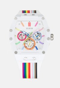 Montre Guess blanche avec bracelet en silicone rayé arc-en-ciel, index colorés et trois sous-cadrans multicolores affichant la date et le jour de la semaine.