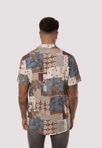 Camisa de manga corta con un diseño de patchwork en azul, crema y marrón que incluye patrones de paisley y geométricos, elaborada con un tejido ligero.
